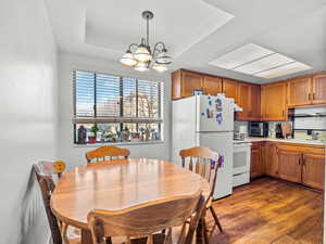 Dining area with dark wood-style floors, hanging lights, and a tray ceiling