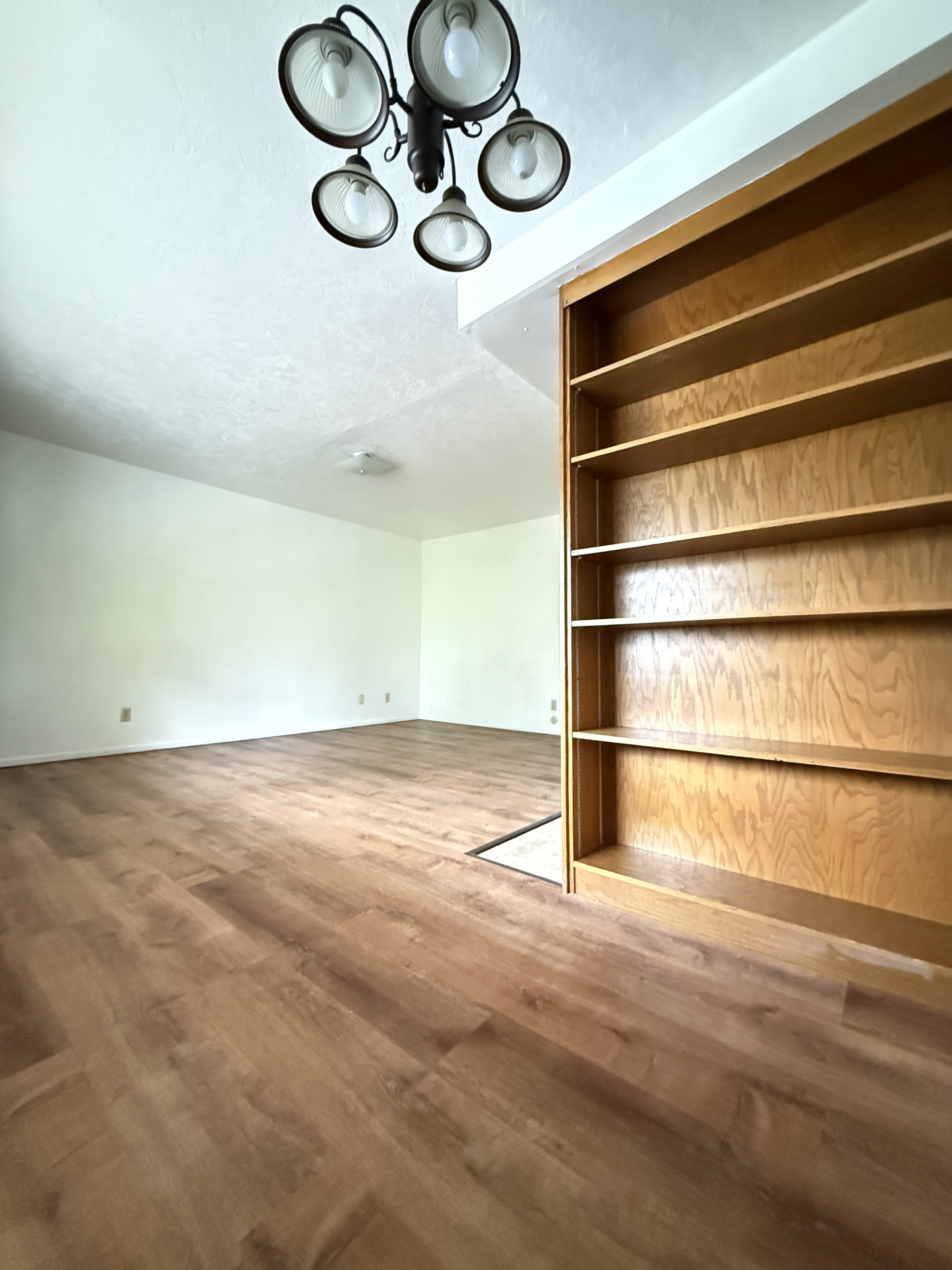 Spacious room featuring wood-finish flooring and a multi-light chandelier
