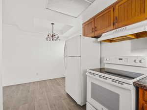 Kitchen with white appliances, light wood-style floors, a chandelier, wood finish cabinetry, and a raised ceiling