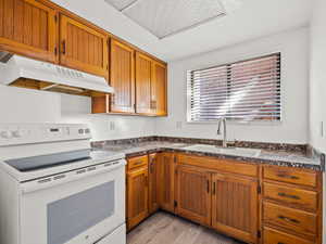 Kitchen featuring white range with electric stovetop, dark countertops, light wood-type flooring, and wood finish cabinets