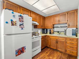 Kitchen featuring white appliances, light countertops, dark wood finished floors, and wood finish cabinets