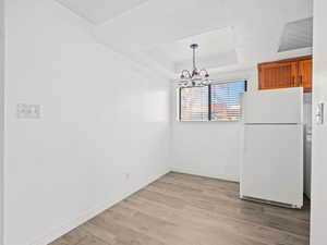 Unfurnished dining area featuring light wood-type flooring, a chandelier, and a raised ceiling