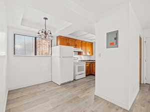 Kitchen with wood finish cabinetry, white appliances, light wood finished floors, electric panel, and suspended lighting
