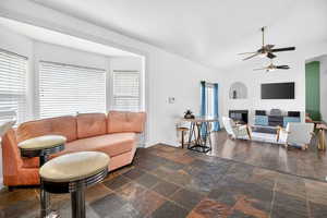 Living room featuring a ceiling fan, stone tile flooring, and vaulted ceiling