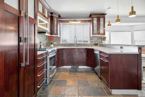 Kitchen with a peninsula, glass fronted cabinets, stainless steel appliances, stone finish floors, and pendant lighting