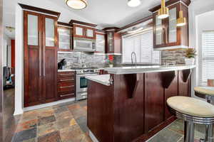 Kitchen featuring stainless steel range oven, a peninsula, dark stone finish flooring, glass fronted cabinets, and a breakfast bar