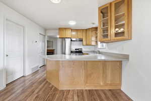Kitchen with light countertops, open shelves, a peninsula, stainless steel appliances, and light wood-style floors
