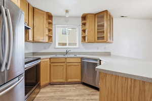 Kitchen with stainless steel appliances, open shelves, light countertops, light wood-style floors, and wood finish cabinetry