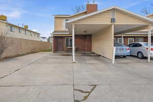 Back of house with brick siding, a chimney, and a carport