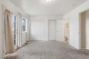 Unfurnished bedroom featuring multiple closets, light carpet, access to exterior, and ensuite bath