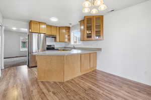 Kitchen featuring light countertops, open shelves, stainless steel appliances, a peninsula, and light wood-style flooring
