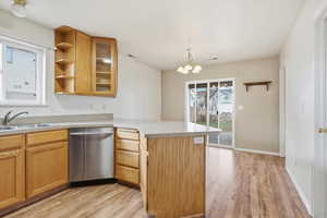 Kitchen featuring a peninsula, open shelves, light countertops, stainless steel dishwasher, and glass fronted cabinets