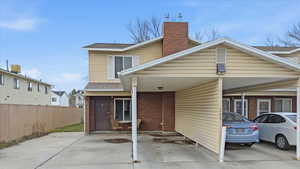 Back of property with a chimney, brick siding, a shingled roof, a carport, and a patio area
