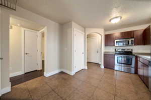 Kitchen featuring stainless steel appliances, arched walkways, a textured ceiling, dark tile patterned floors, and dark wood finish cabinets