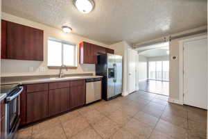Kitchen featuring arched walkways, stainless steel appliances, a textured ceiling, light tile patterned flooring, and light countertops