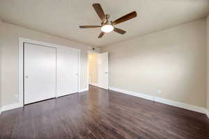 Unfurnished bedroom featuring dark wood-style flooring, a ceiling fan, a closet, and a textured ceiling