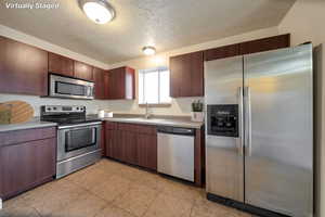 Kitchen with stainless steel appliances, a textured ceiling, light countertops, and light tile patterned floors