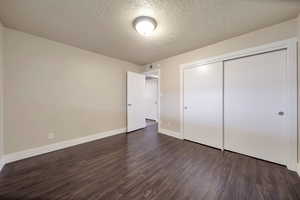 Unfurnished bedroom with dark wood-style flooring, a textured ceiling, and a closet