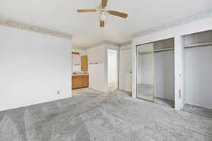 Unfurnished bedroom with light carpet, ensuite bathroom, a ceiling fan, and a closet
