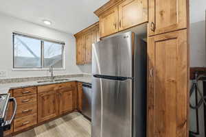 Kitchen featuring stainless steel appliances, light stone counters, wood finish cabinetry, and light wood-style floors