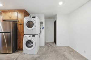 Laundry room with stacked washer and clothes dryer and light colored carpet