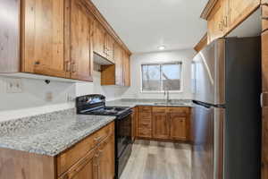 Kitchen with black electric range, freestanding refrigerator, light stone countertops, and wood finish cabinetry