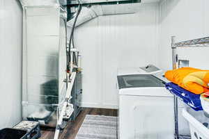 Laundry area with dark wood-type flooring, heating unit, washer and dryer, and wooden walls