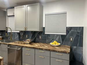 Kitchen featuring gray cabinetry, dishwasher, wooden counters, and decorative backsplash