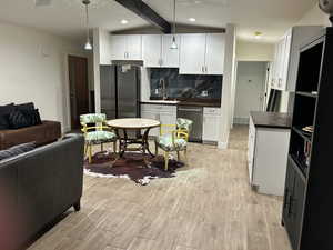 Kitchen with white cabinetry, wood finish floors, stainless steel appliances, vaulted ceiling with beams, and backsplash