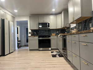 Kitchen with gray cabinets, range with electric stovetop, freestanding refrigerator, tasteful backsplash, and stainless steel microwave