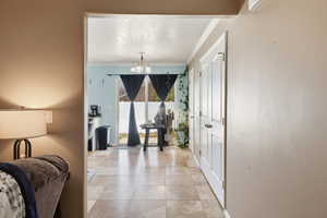 Hall with crown molding, a chandelier, and light tile patterned floors