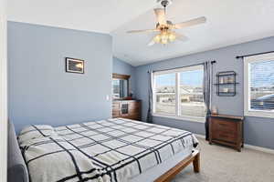 Bedroom featuring vaulted ceiling, light carpet, ceiling fan, and multiple windows