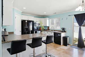 Kitchen with dark countertops, a peninsula, a breakfast bar area, black appliances, and white cabinets