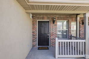 Entrance to property featuring a porch, brick siding, and stucco siding