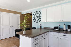 Kitchen with a peninsula, dark countertops, white cabinets, a breakfast bar, and ornamental molding