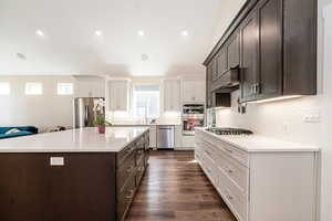 Kitchen with two tone cabinetry, stainless steel appliances, light stone countertops, recessed lighting, and a kitchen island