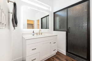 Full bath featuring vanity, dark wood-style flooring, a stall shower, and a walk in closet