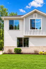 View of property exterior featuring stone siding, a yard, board and batten siding, and roof with shingles