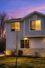 Property exterior at dusk featuring board and batten siding, a yard, and stone siding