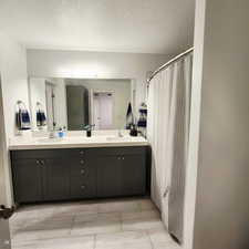 Primary Bathroom with double vanity, a shower with shower curtain, and a textured ceiling