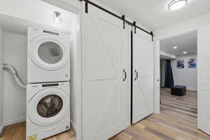 Laundry area with a barn door, light wood-style flooring, and stacked washer and clothes dryer