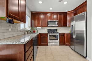 Kitchen featuring light stone counters, stainless steel appliances, recessed lighting, light tile patterned floors, and decorative backsplash