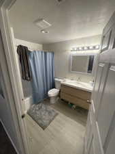 Full bathroom featuring vanity, light wood finished floors, shower / bath combo with shower curtain, and a textured ceiling