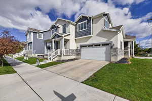 View of front facade with stucco siding, a front lawn, stone siding, and driveway