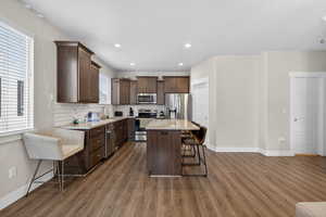 Kitchen featuring dark wood finish cabinets, stainless steel appliances, a kitchen breakfast bar, backsplash, and light stone countertops