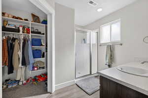 Bathroom featuring a stall shower, vanity, light wood-style flooring, and a walk in closet