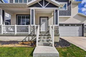 View of exterior entry with stucco siding, covered porch, stone siding, and driveway