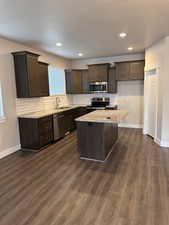 Kitchen featuring dark wood finish cabinets, light stone counters, stainless steel appliances, tasteful backsplash, and recessed lighting