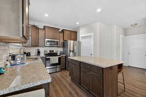 Kitchen with a center island, stainless steel appliances, light stone counters, dark wood-type flooring, and a breakfast bar