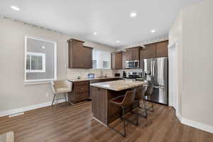 Kitchen with a kitchen island, stainless steel appliances, a breakfast bar area, light stone countertops, and dark wood finish cabinetry